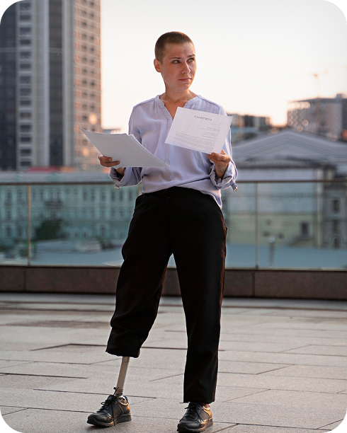Mujer profesional usando prótesis de pierna sosteniendo documentos frente a edificios de la ciudad