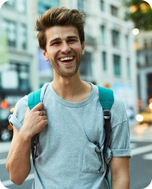 Joven hombre con mochila azul sonriendo en un ambiente urbano, listo para trabajar