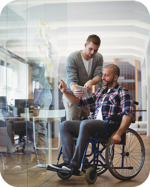 Hombre profesional enseñando a un joven en silla de ruedas en una oficina con pizarra de vidrio, ambiente inclusivo de trabajo